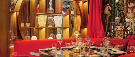 Un espace repas agrémenté d’un lustre, de sièges recouverts d’un tissu rouge et d’éléments décoratifs en bois.