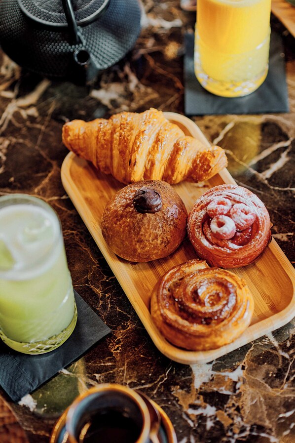 A breakfast setting with a croissant, a muffin, and a cinnamon roll on a wooden board. - Maya Hotel Courchevel 1850 (Courchevel)