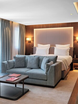 Habitació d'hotel moderna amb un llit gran, un sofà gris, una taula petita i una tauleta de nit.