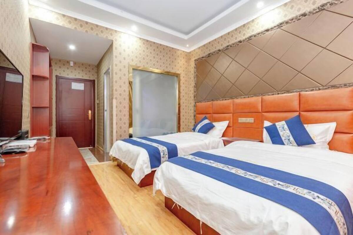 Quarto de hotel com duas camas, uma escrivaninha de madeira e um papel de parede estampado.