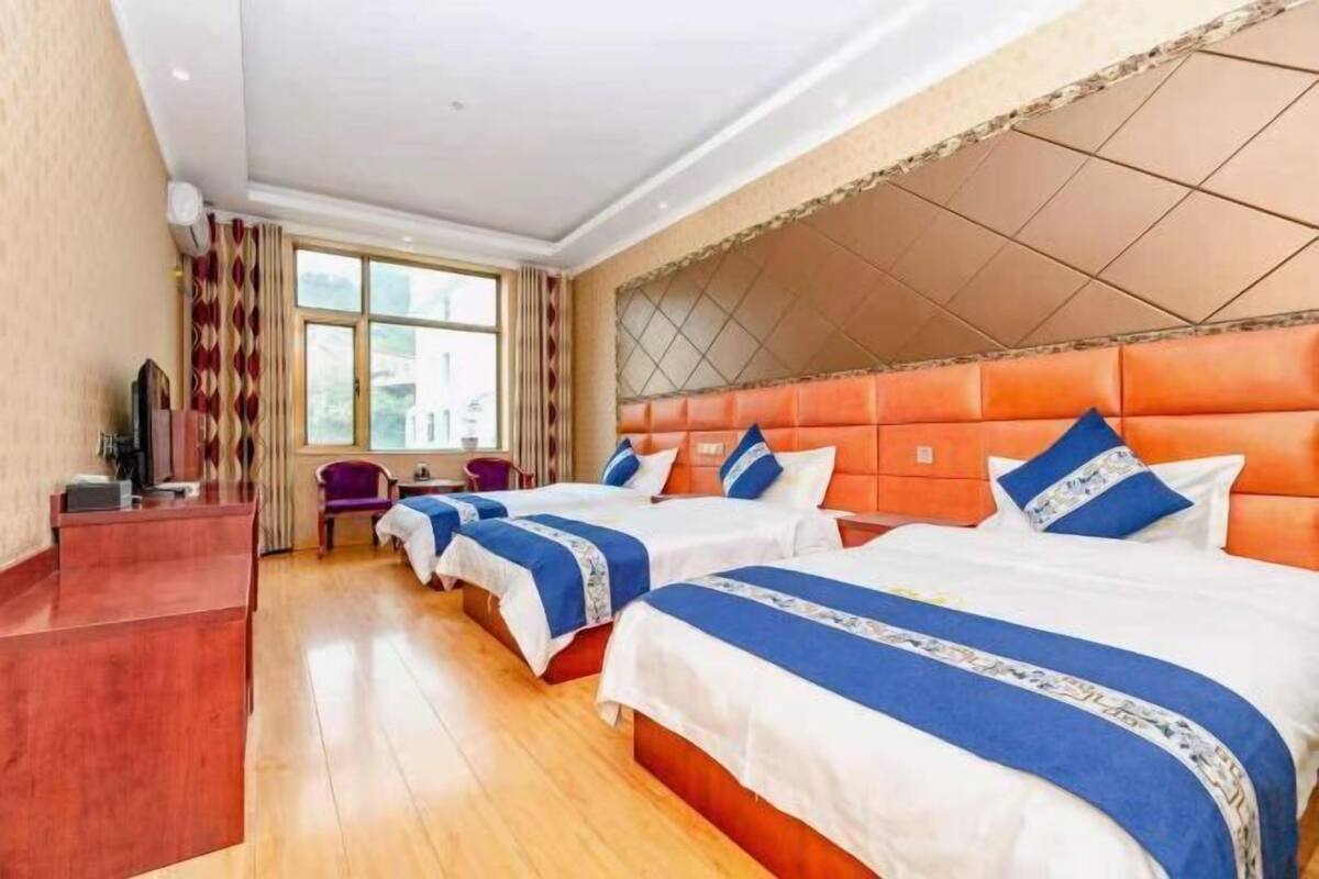 Quarto de hotel com quatro camas, uma mesa de recepção, televisão e uma janela com cortinas.