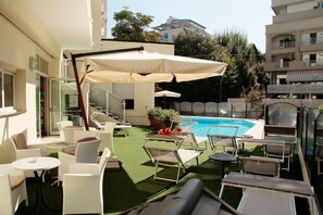 A rooftop pool area with lounge chairs and umbrellas, surrounded by greenery and buildings. - Bellevue (Cattolica)