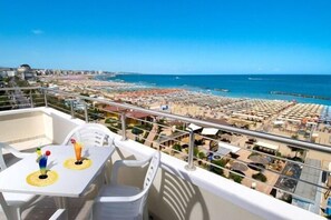 A balcony with a table and chairs overlooking a beach and cityscape. - Bellevue (Cattolica)