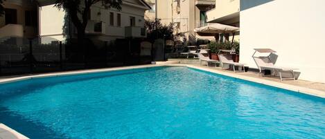 A swimming pool with lounge chairs and a building in the background.