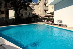 A swimming pool with lounge chairs and a building in the background. - Bellevue (Cattolica)