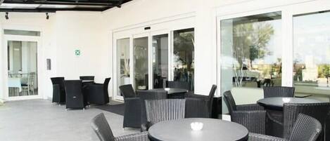 A covered outdoor seating area with wicker furniture and glass doors leading to an interior space.
