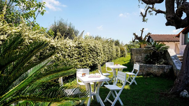 Een tuin met witte tafels en stoelen, omringd door weelderig groen en een stenen muur.