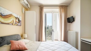 Een slaapkamer met een bed, een schilderij, een televisie en een schuifdeur naar buiten.