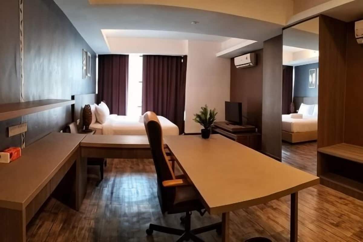 A hotel room with a bed, a desk, a chair, a television, and a small table.