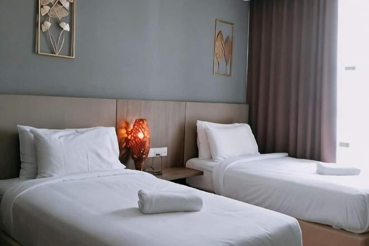A hotel room with two beds, a nightstand, a lamp, and a window with curtains.