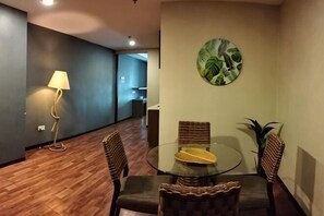 Un'area pranzo con un tavolo rotondo in vetro, sedie in vimini, una lampada a parete e un quadro a tema tropicale.
