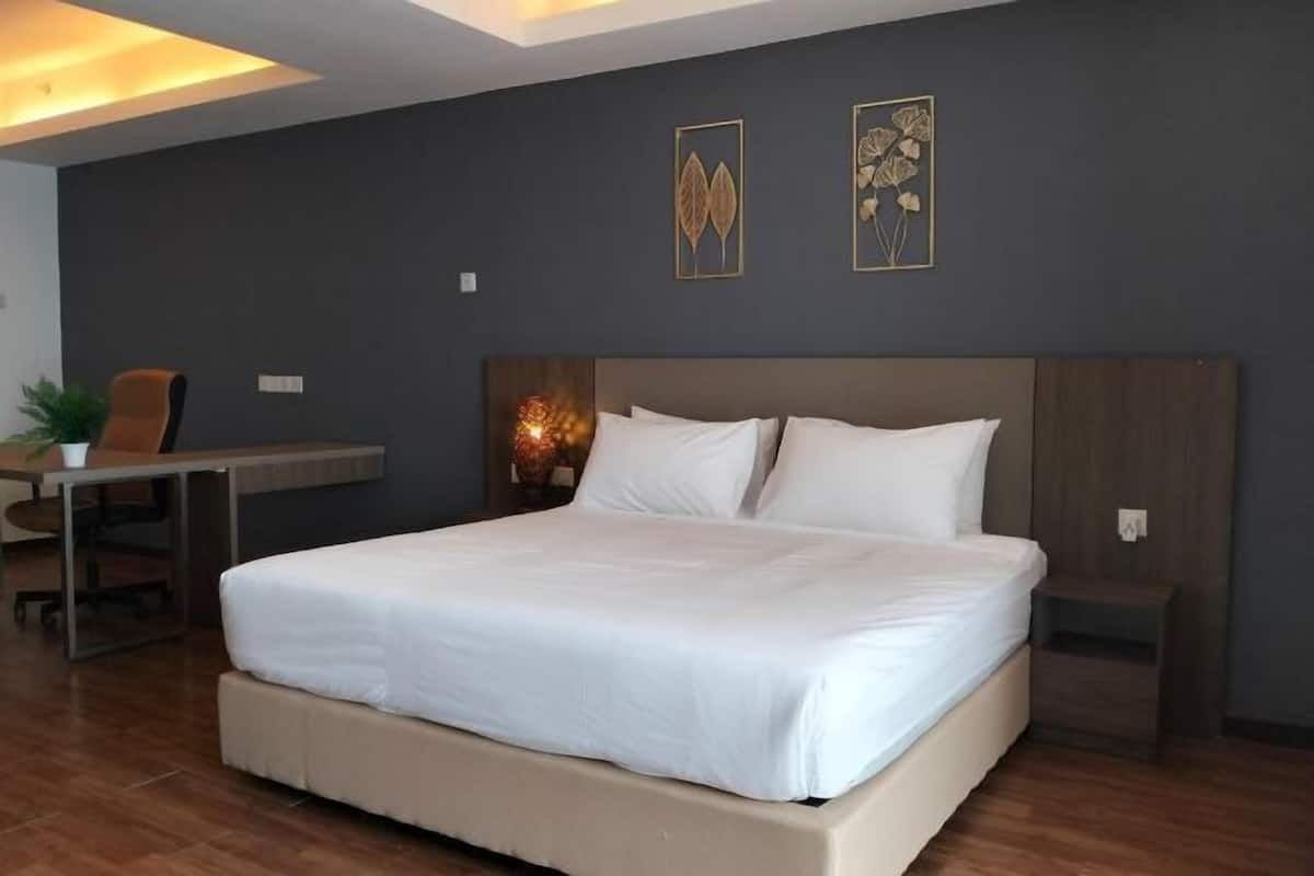 Moderni hotellihuone, jossa on suuri sänky, työpöytä ja kaksi kehystettyä taideteosta seinällä.