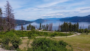 A lakeside view with a clear sky, surrounded by trees and a distant mountain range.