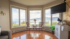 Ein Essbereich mit Tisch und Stühlen, große Fenster mit Blick, eine Küchenzeile und ein flachbildfernseher an der Wand.