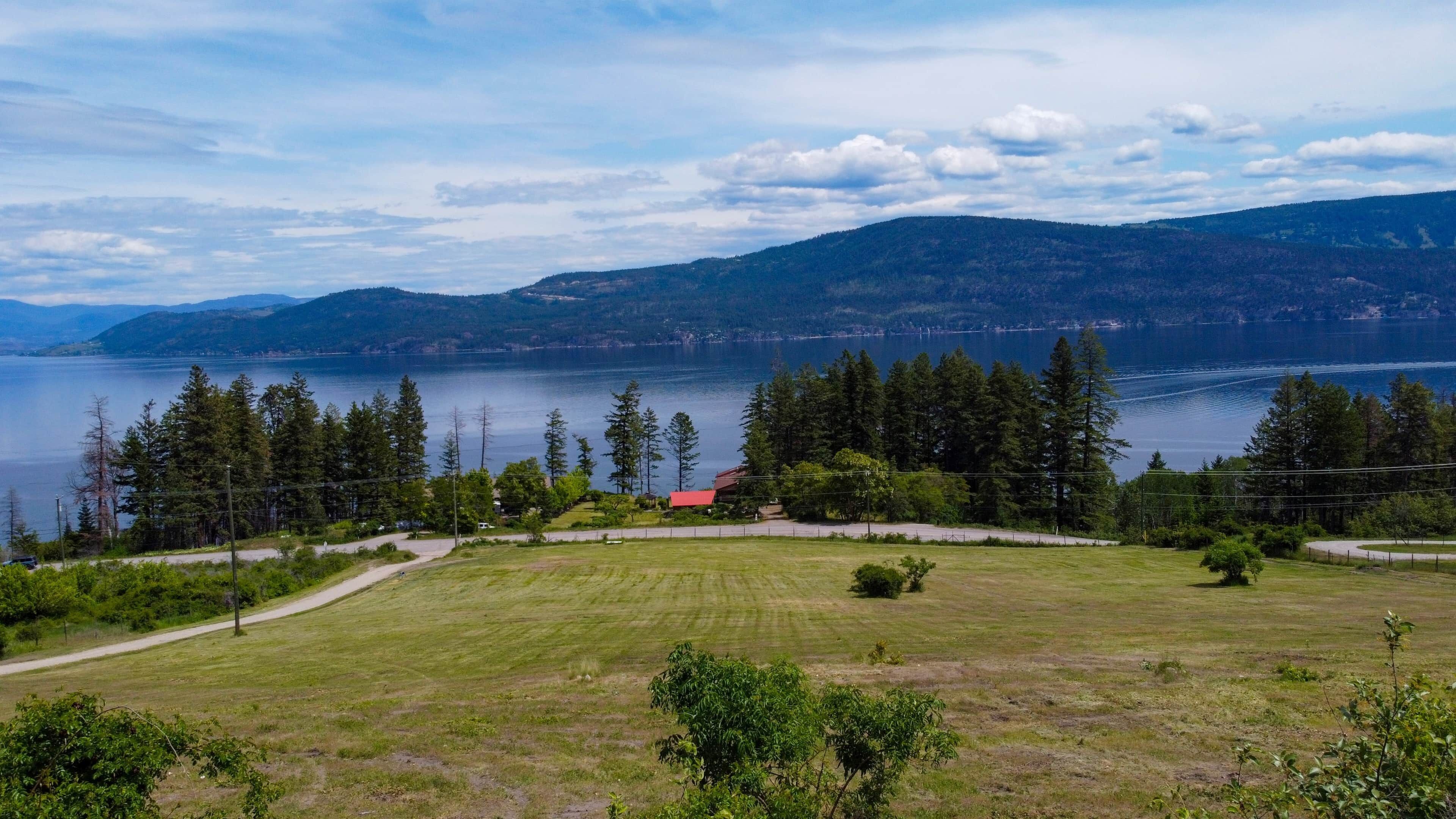 A grassy field with a red-roofed building, surrounded by trees and a lake.