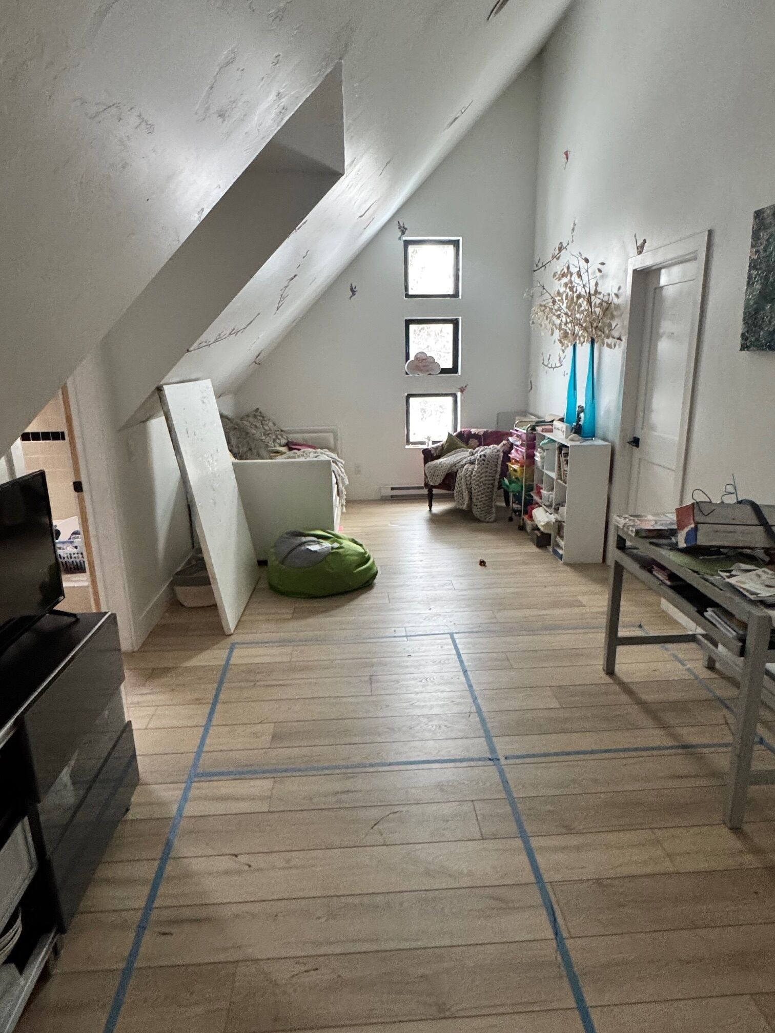 A loft-style room with a sloped ceiling, a green bean bag chair, a white couch, and a small table with various items.