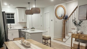A modern kitchen with white cabinets, a central island, and a dining area with wooden furniture.