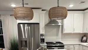 A modern kitchen with white cabinetry, a stainless steel refrigerator, a built-in oven, and a central island with stools.