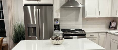 A modern kitchen with white cabinetry, a stainless steel refrigerator, a built-in oven, and a central island with stools.