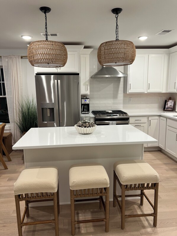 Una cocina moderna con armarios blancos, un refrigerador de acero inoxidable, horno empotrado y una isla central con taburetes.