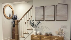 A staircase with a wooden finish, a console table with baskets, and three framed artworks on the wall.
