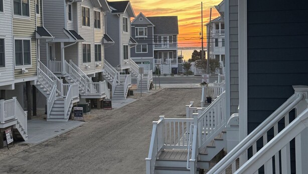 A row of beach houses with a sandy driveway and a staircase leading to the entrance.