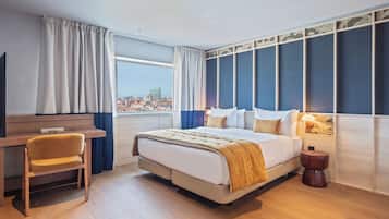 A modern hotel room with a large bed, a desk, and a view of the city.