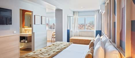 Une chambre d’hôtel moderne dotée d’un grand lit, d’un coin salon, d’une salle de bain avec un miroir et offrant une vue sur la ville.