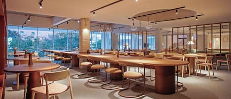 A modern dining area with round tables and chairs, large windows, and a view of the outdoors.