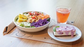 Un plato con ensalada, una porción de pastel de queso y un vaso de bebida sobre una mesa de madera.