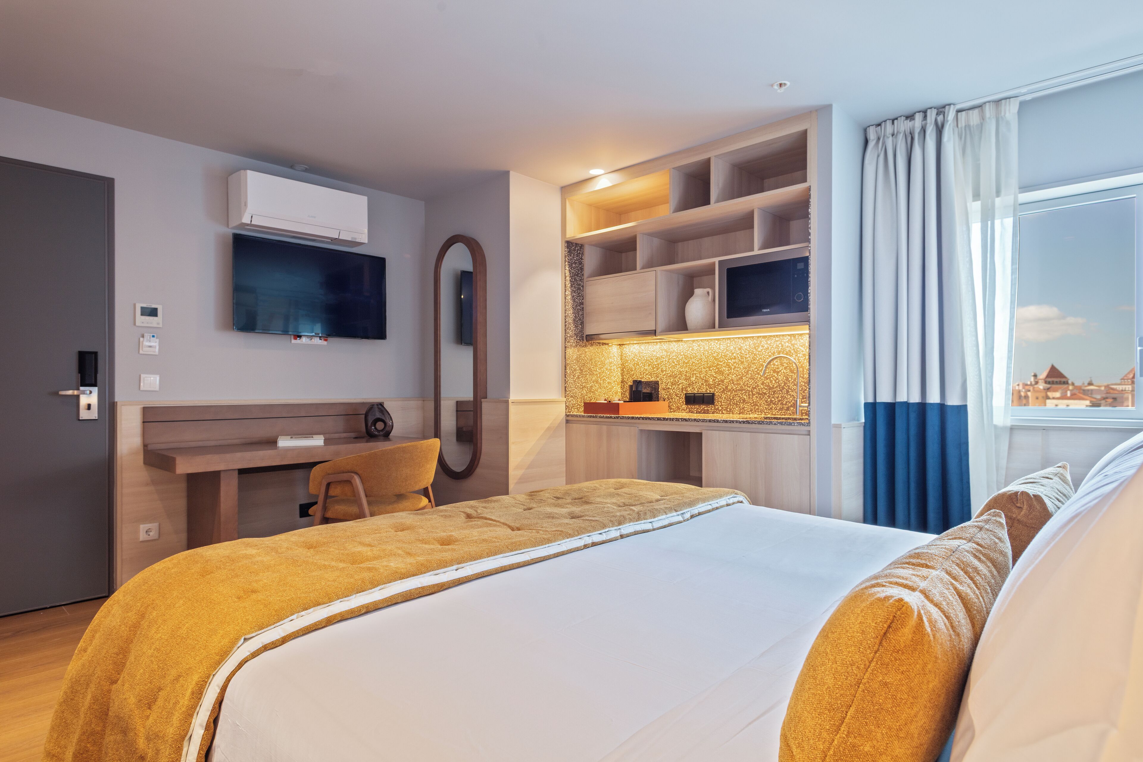 Een hotelkamer met een bed, een bureau, een televisie, een spiegel en een raam met gordijnen.
