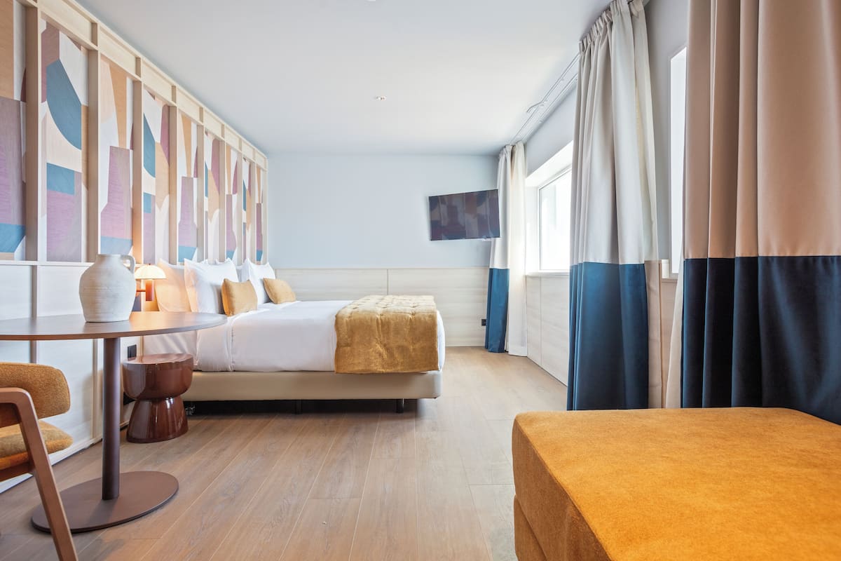 A modern hotel room with a bed, a table, a chair, and a TV on the wall.