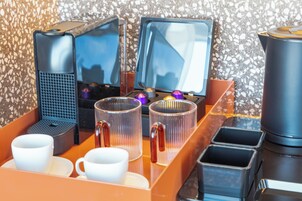 A coffee station with a coffee maker, two screens, and a trash bin.