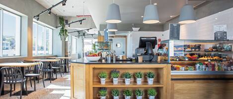 A modern cafe interior with wooden tables, chairs, and a counter displaying pastries and drinks.
