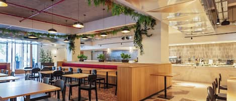 Un intérieur de restaurant moderne, avec de nombreuses tables, des banquettes et un espace cuisine.