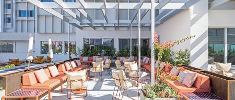 An outdoor seating area with multiple tables and chairs, a sofa, and a planter with flowers.