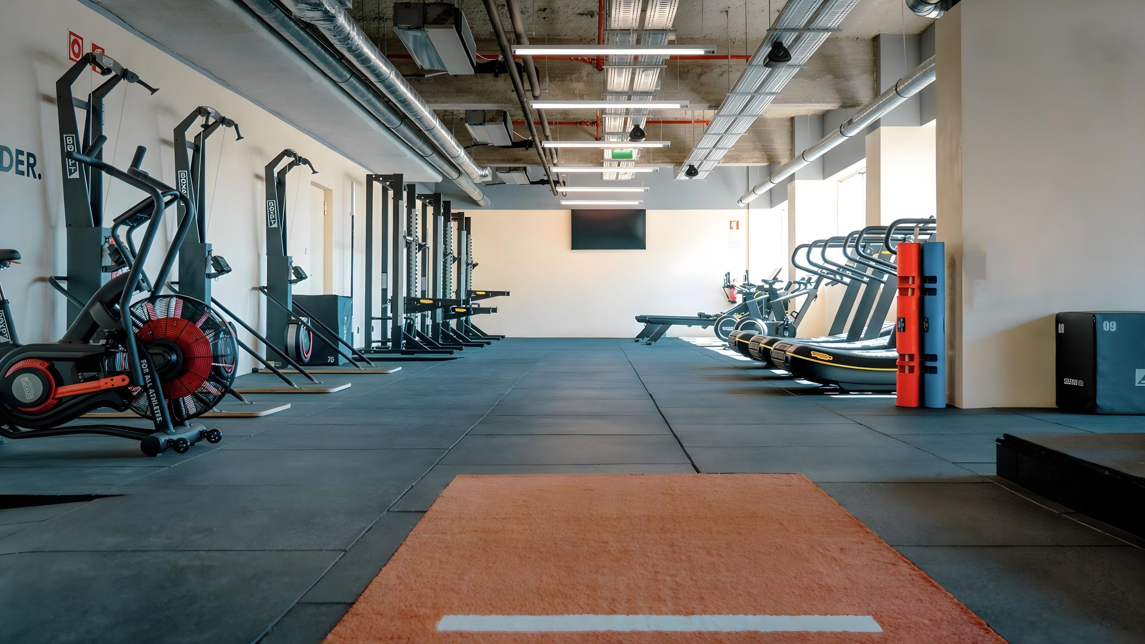 A gym with various exercise equipment, including treadmills and weight machines, arranged in rows.
