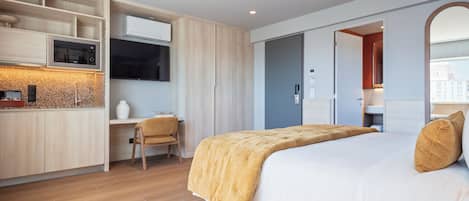 A modern hotel room with a bed, a desk, and a kitchenette.