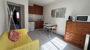 Un ambiente compatto con angolo cottura, zona pranzo e salotto con divano giallo.