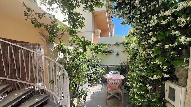 Un cortile con una scala a chiocciola bianca, una pianta in vaso, un tavolo rotondo con tovaglia floreale e una statua di pietra.