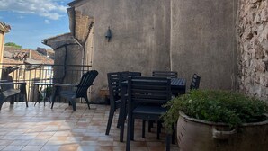 An outdoor patio with tiled flooring, black metal chairs, and a large potted plant.