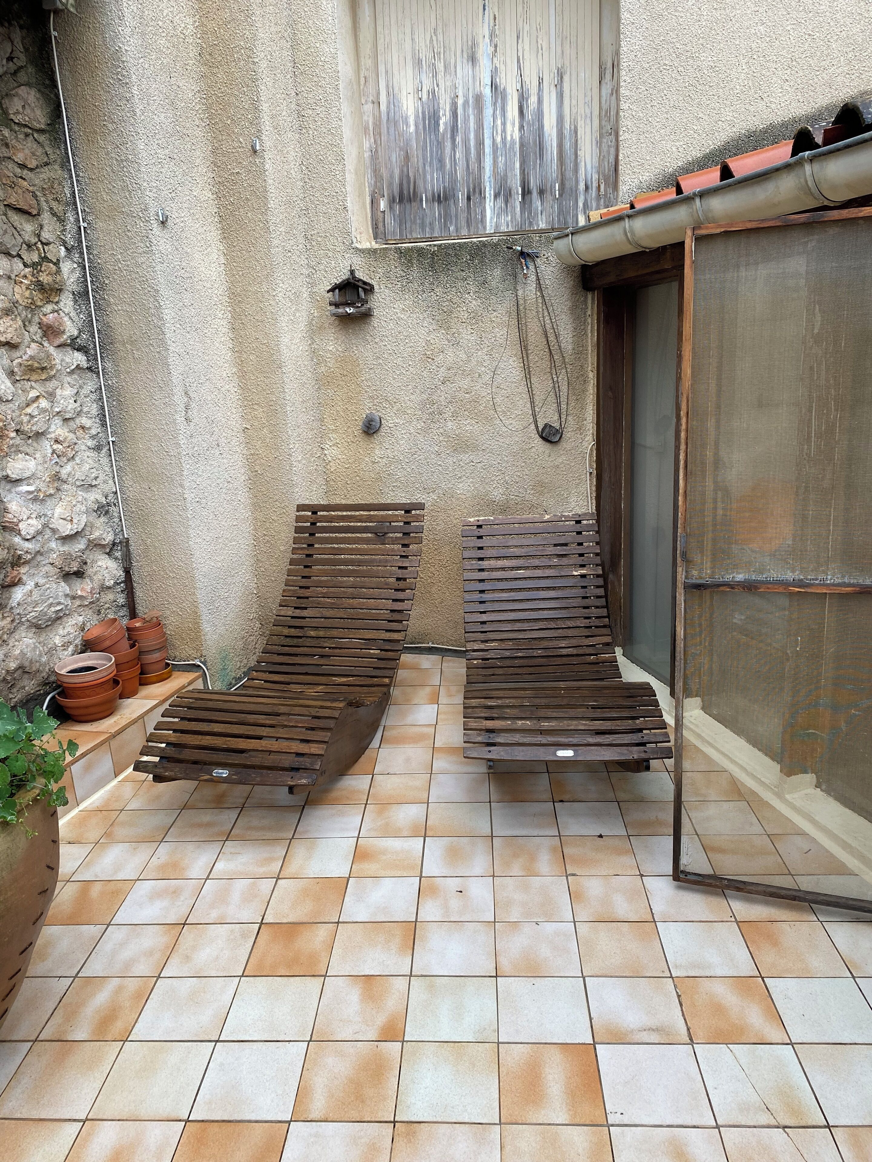 Une petite terrasse extérieure avec deux chaises longues en bois, un sol carrelé et des pots en terre cuite.