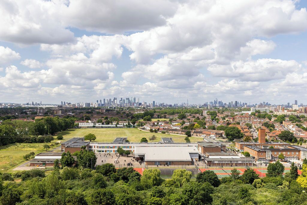 A large building with multiple sports fields and a city skyline in the background.