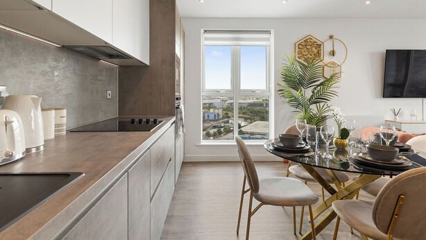 A modern kitchen with a dining area, large windows, and a view of the city. - The Lasgidi - One Bed (Barking)