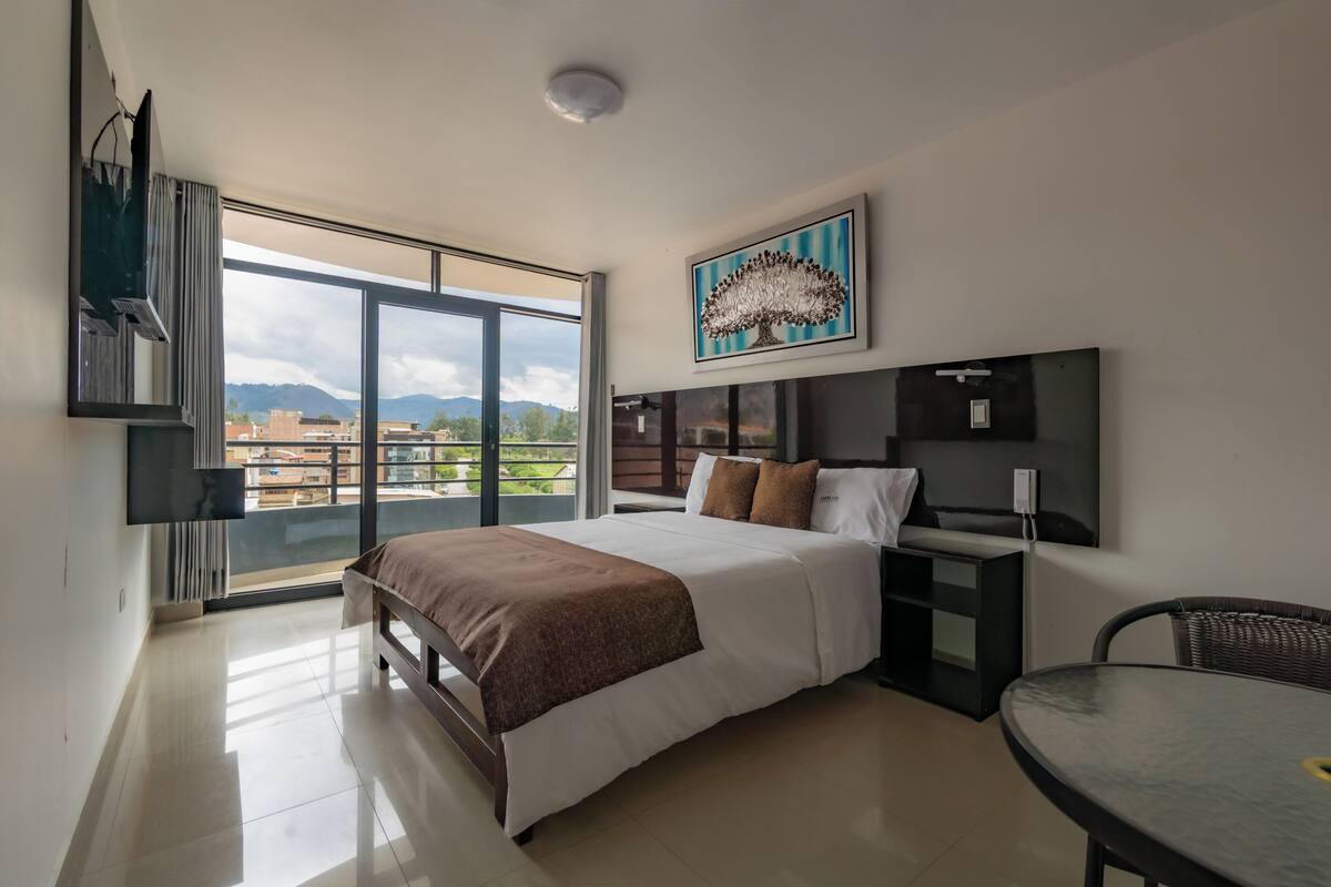 Una habitación de hotel moderna con una cama grande, un escritorio y un balcón con vistas a la ciudad.