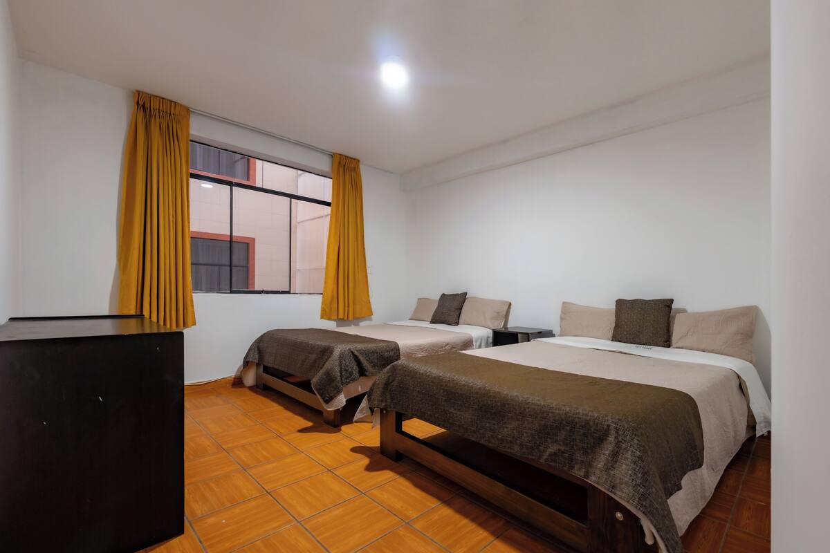 Una habitación con dos camas individuales, un aparador de madera y una ventana con cortinas.