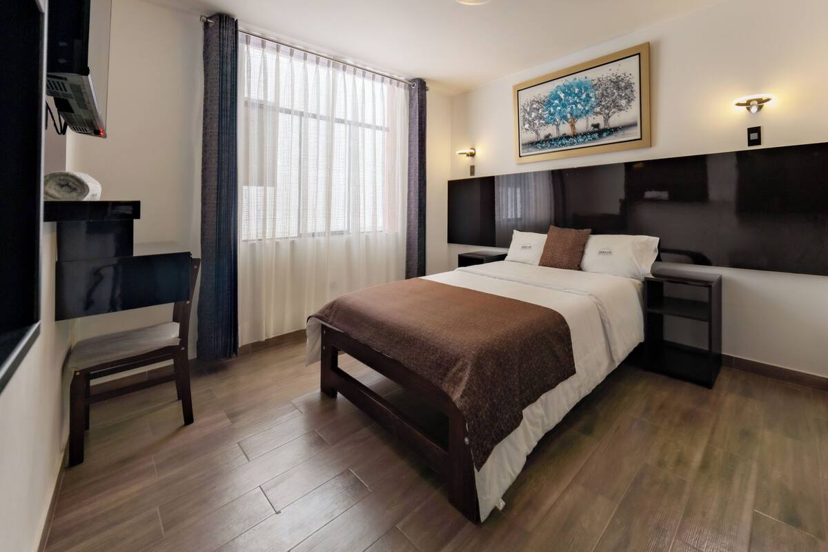 Una habitación de hotel moderna con cama, mesitas de noche, un escritorio y una ventana con cortinas.