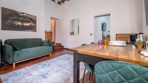 A spacious living room with a wooden dining table, a green sofa, and a large abstract painting on the wall.
