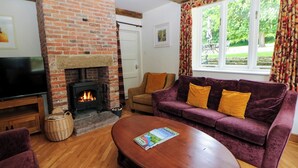 Una sala de estar acogedora con chimenea de ladrillo, un sofá con cojines amarillos, una mesa de centro de madera y un televisor sobre un mueble de madera.