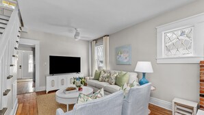 A modern living room with a white sofa, a coffee table, and a television. There is a small white table and a lamp on the right side. - 3 bed/2 BA house in great Augusta area w/Wi-Fi, AC, and many restaurants nearby (Augusta)